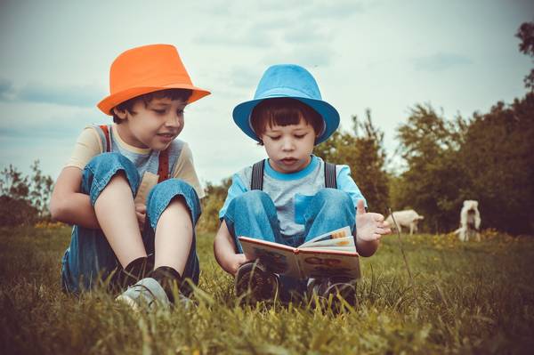Zwei Kinder sitzen auf der Wiese und lesen ein Buch