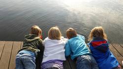 Quelle: pixabay.de / EME, https://pixabay.com/de/photos/kinder-m%C3%A4dchen-jungen-liegen-516340/ Vier Kinder liegen auf Steg und beobachten das Wasser